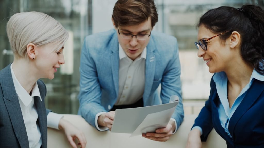 Home Close-up of cheerful businessman talking and discussing about financial report with business female colleagues sitting on sofa in meeting room indoors